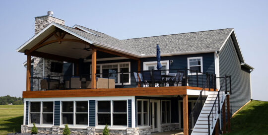 exterior of blue house with large balcony deck with sunroom below